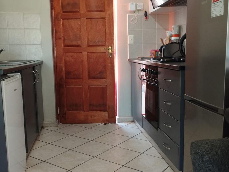 A functional kitchen featuring built-in cabinetry, a fitted oven and hob, extractor fan, and tiled flooring with a rear access door.