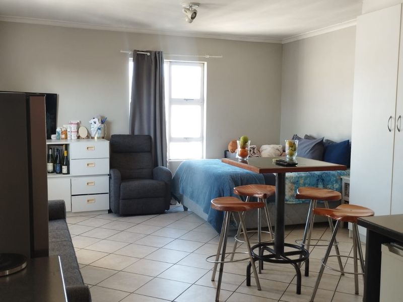An open-plan studio apartment featuring tiled flooring, built-in wardrobe storage, and ceiling-mounted spotlights, offering a functional living and sleeping space.