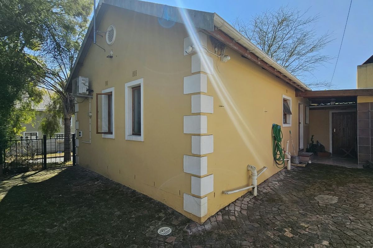 Rear exterior view of the house featuring paved ground, security fencing, and wall-mounted air conditioning unit.