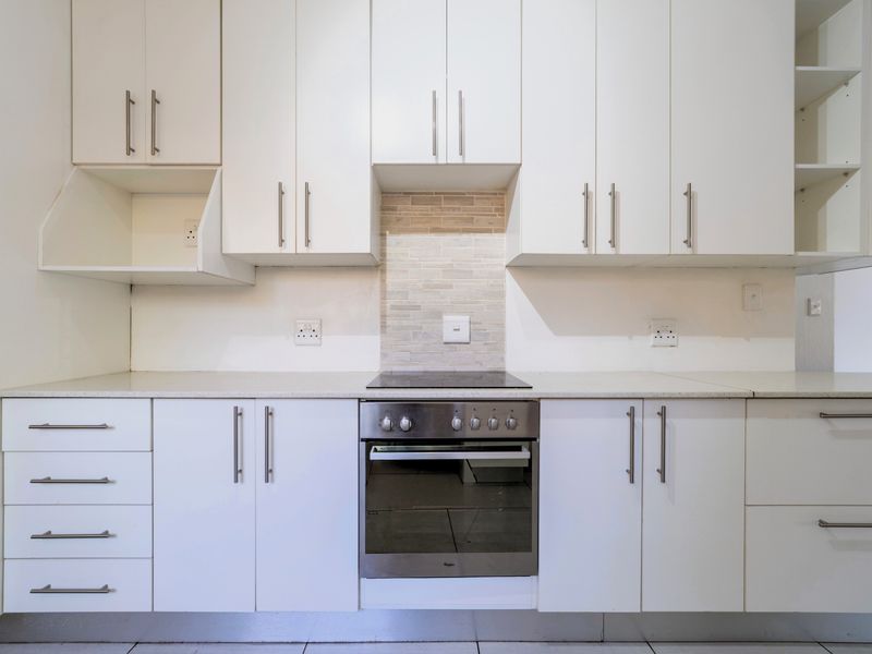 A clean, modern kitchen featuring white cabinetry, stone countertops, a tiled backsplash, and a built-in electric oven and hob.