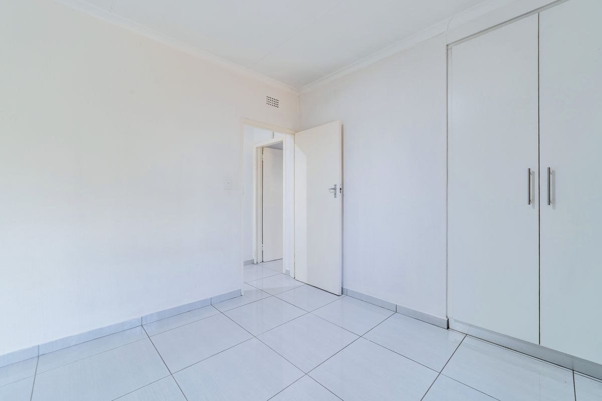 A bright, empty bedroom featuring neutral tiled flooring and a built-in wardrobe, offering a clean canvas for personalization.