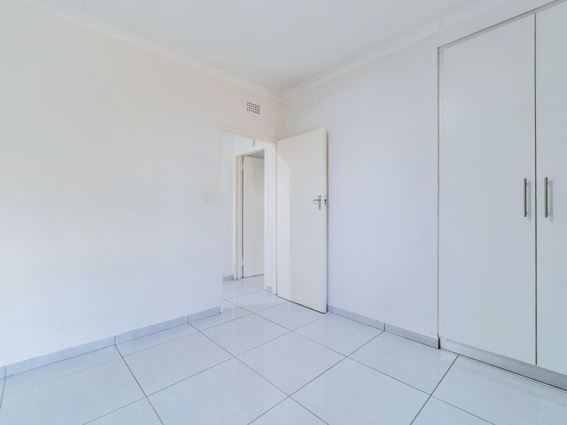 A bright, empty bedroom featuring neutral tiled flooring and a built-in wardrobe, offering a clean canvas for personalization.