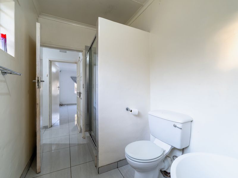 A functional bathroom featuring a shower enclosure, toilet, and tiled flooring, presenting a clean, neutral space ready for potential cosmetic updates.