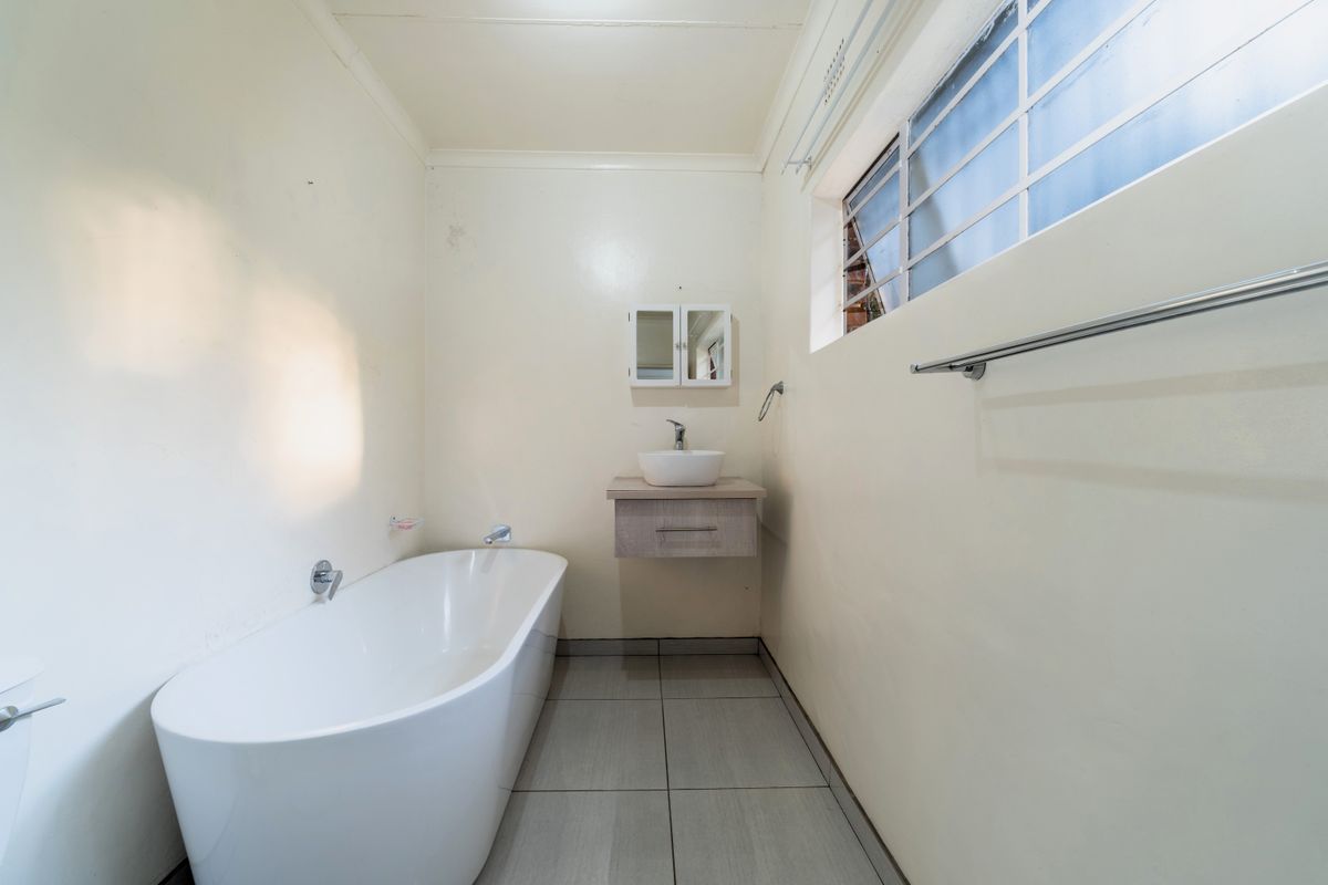 A clean, minimalist bathroom featuring a modern freestanding bathtub, a wall-mounted vanity with a vessel sink, and neutral tiled flooring.