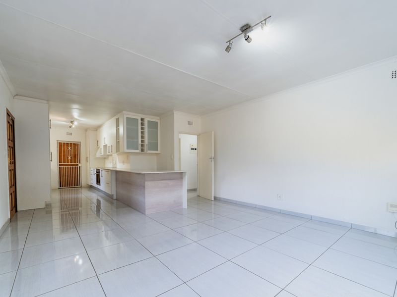 Spacious open-plan living area featuring tiled flooring, modern kitchen cabinetry with a breakfast island, and built-in oven, offering a clean and versatile layout.