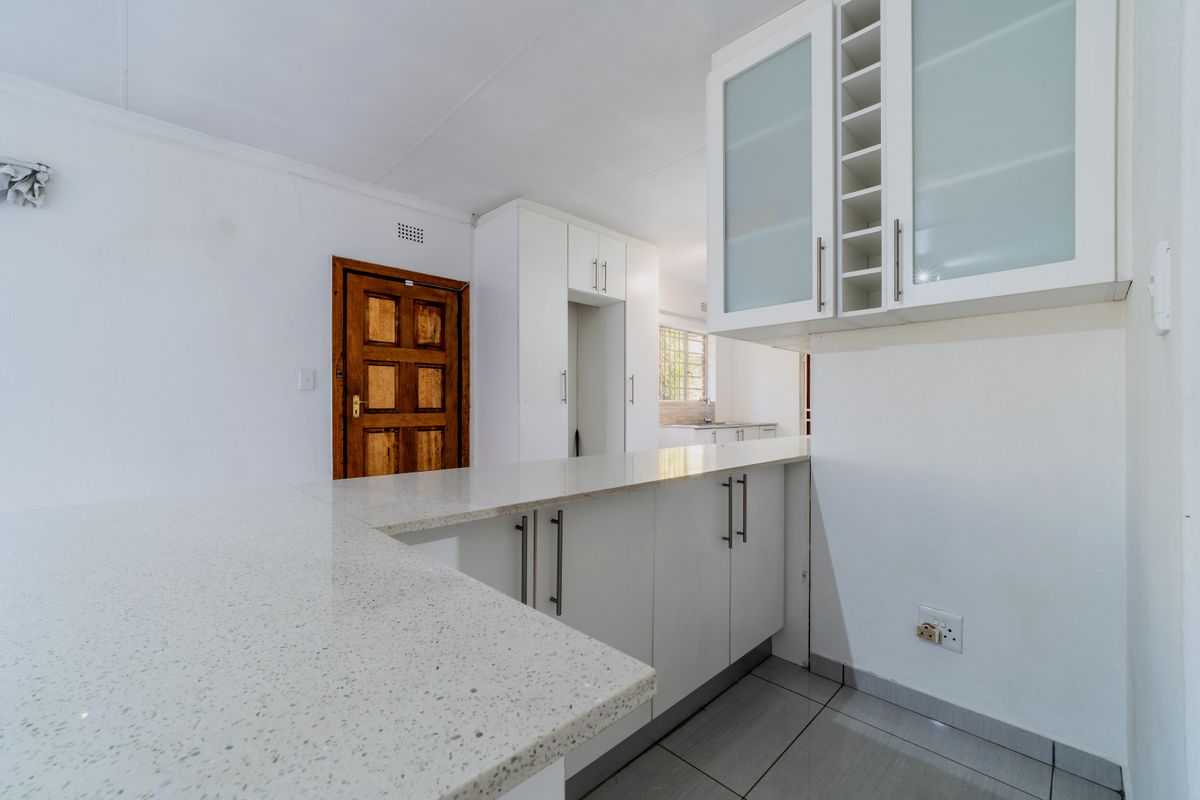 A clean, modern kitchen featuring white cabinetry, stone countertops, and tiled flooring, with a view through to a secondary prep area.