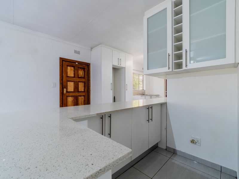 A clean, modern kitchen featuring white cabinetry, stone countertops, and tiled flooring, with a view through to a secondary prep area.