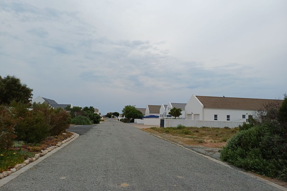 A view of a gravel residential street lined with white houses and boundary walls in a quiet neighborhood setting.