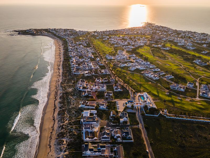 An expansive aerial view of a coastal residential estate featuring a golf course, beach access, and well-maintained properties at sunset.