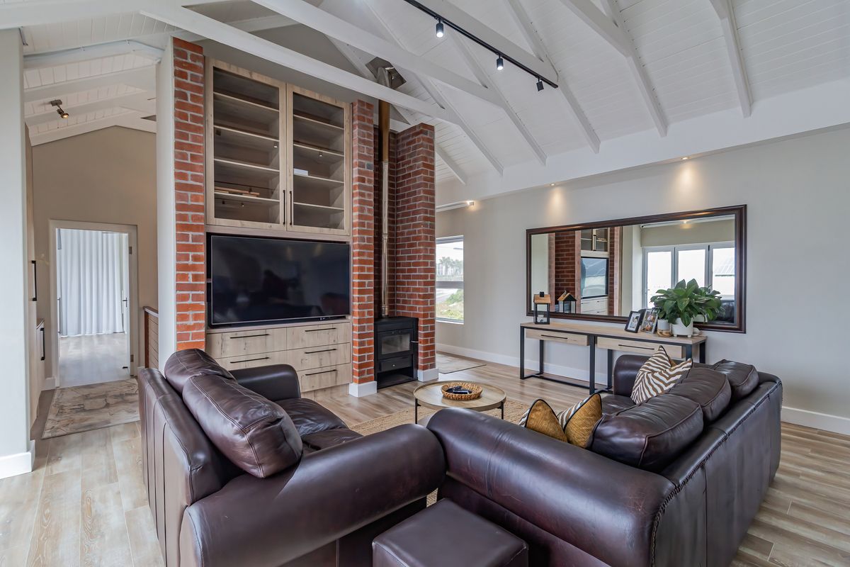 Spacious living room featuring a vaulted ceiling with exposed rafters, a striking exposed brick fireplace with a wood-burning stove, and custom built-in cabinetry.