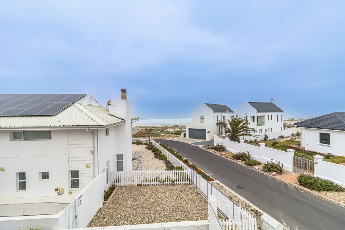 An elevated view of a coastal residential street featuring modern homes with metal roofs, solar panels, and well-maintained boundary walls and fencing.