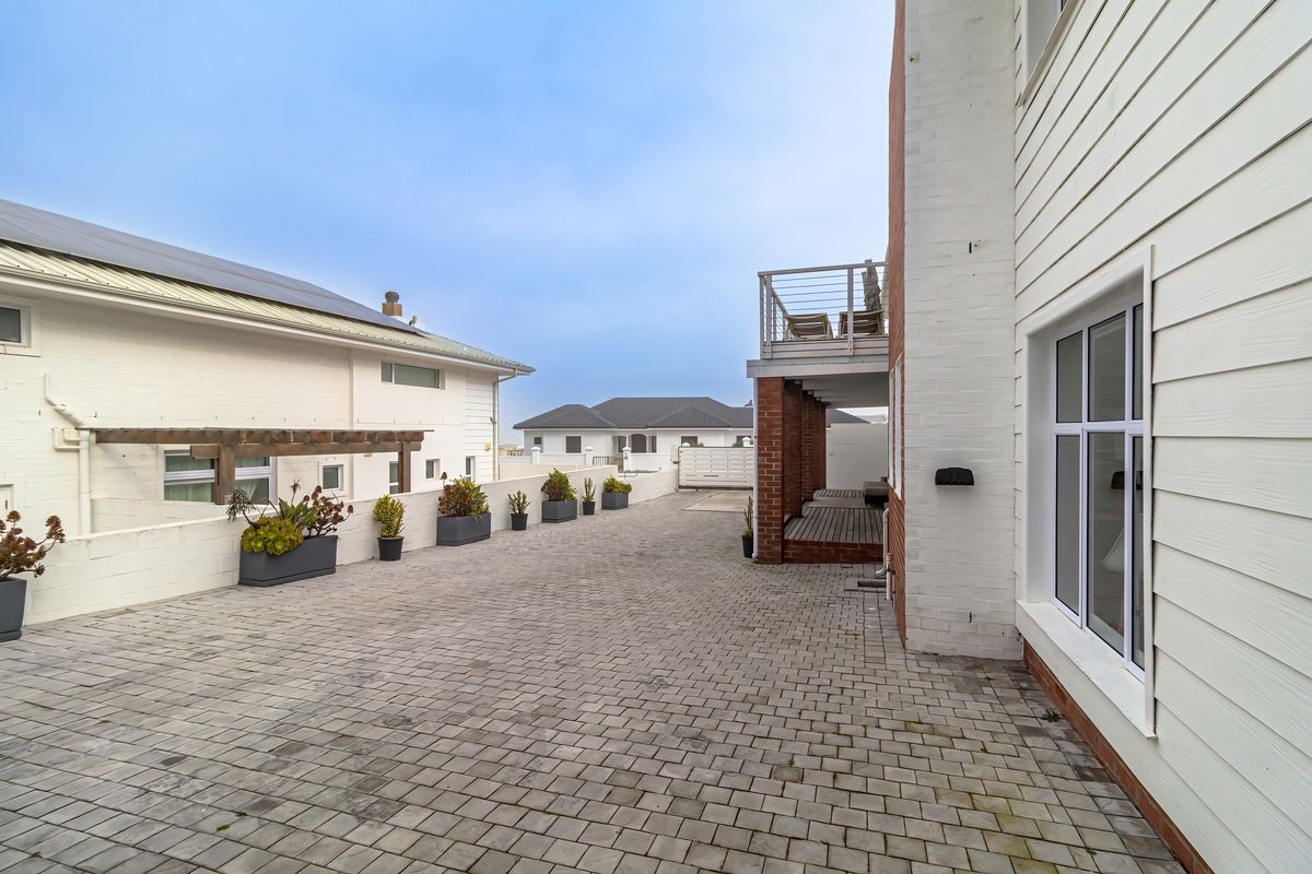 A well-maintained rear exterior area featuring paved driveway, timber pergola, and a balcony overlooking the property.