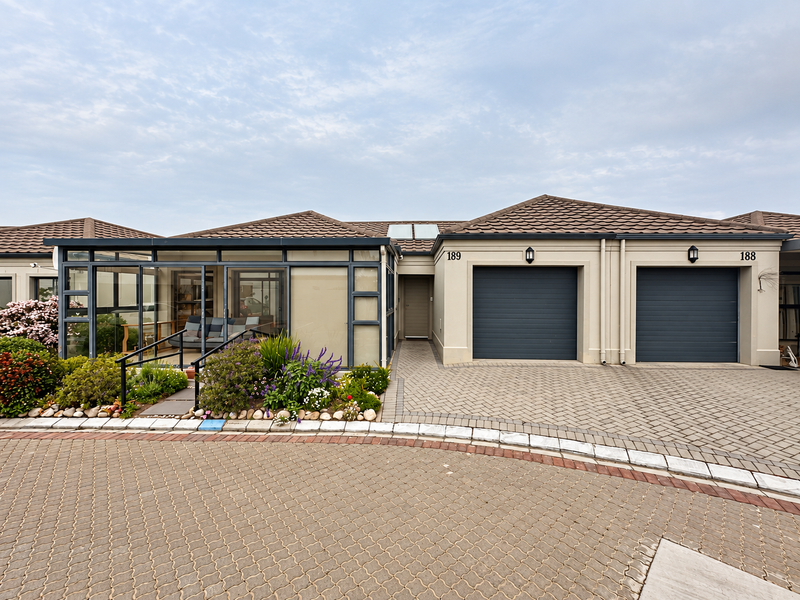 Front view of a townhouse featuring a paved driveway, double garage, and an enclosed sunroom with large glass panels.