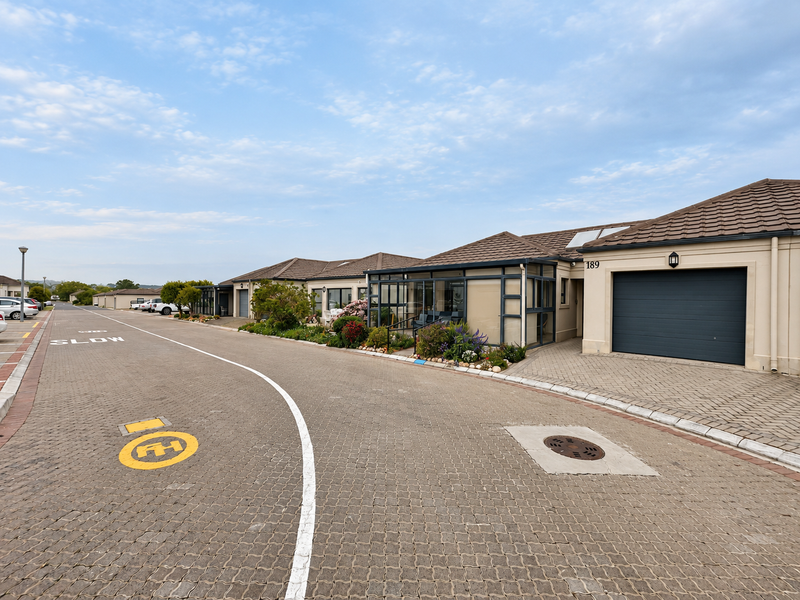 A street-level view of a residential townhouse complex featuring paved driveways, enclosed patios, and individual garage access.