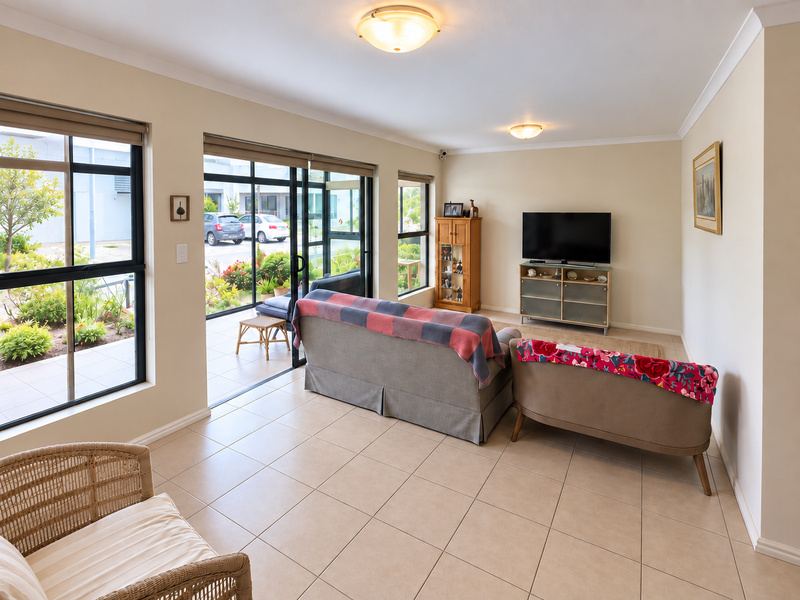 A bright living room featuring tiled flooring, large windows, and sliding glass doors that provide direct access to the outdoor patio area.