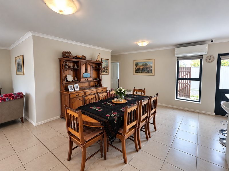 A well-maintained dining area featuring neutral tiled flooring, cove cornicing, and a wall-mounted split-system air conditioner for climate control.