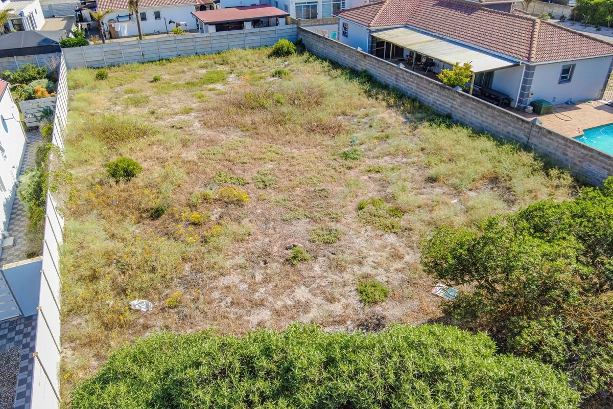 An aerial view of a vacant residential plot enclosed by boundary walls, featuring natural vegetation and surrounding residential properties.