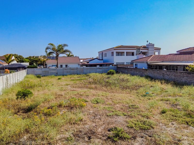A vacant residential plot enclosed by precast concrete boundary walls, featuring natural ground cover and surrounding established residential properties.