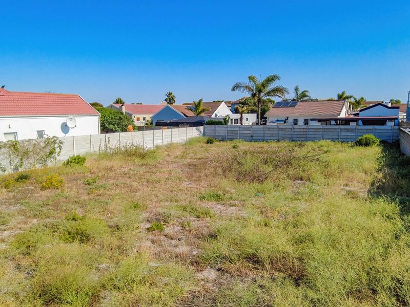 A vacant residential plot enclosed by precast concrete boundary walls, situated in a developed suburban neighborhood.