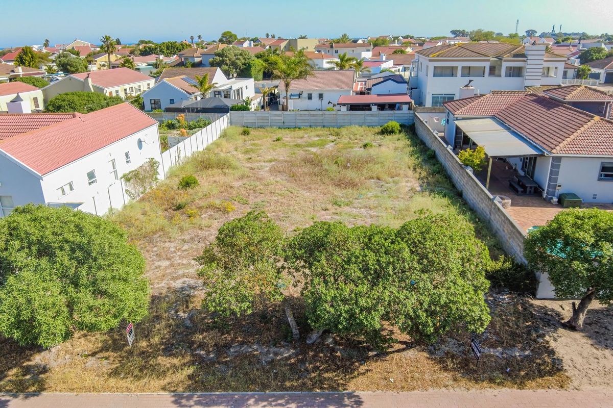 An aerial view of a vacant residential plot situated in a developed neighborhood, featuring boundary fencing and established trees on the property.