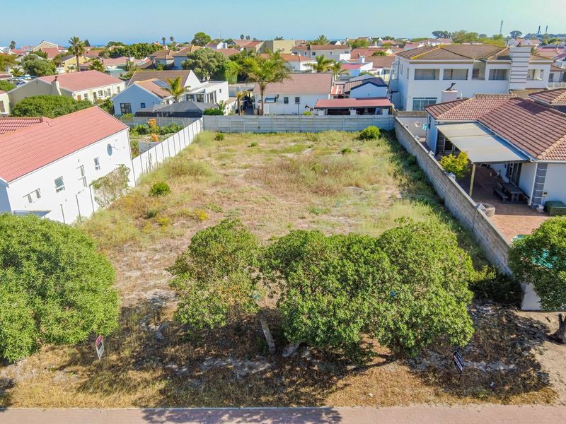 An aerial view of a vacant residential plot situated in a developed neighborhood, featuring boundary fencing and established trees on the property.