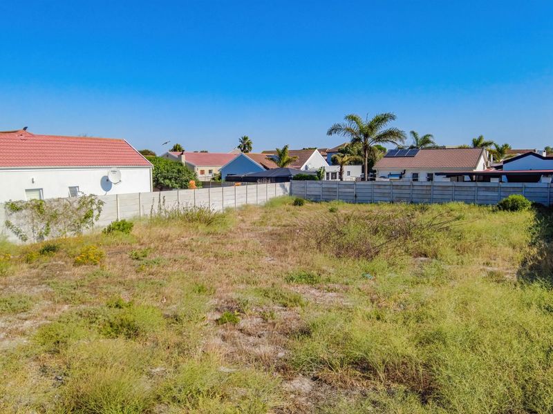 A vacant residential plot enclosed by precast concrete boundary walls, featuring natural ground cover and surrounding suburban residential properties.