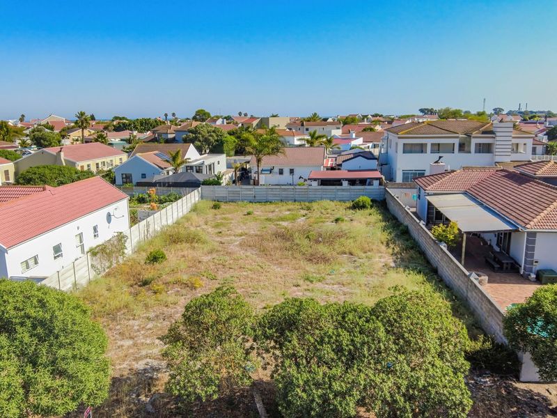 An aerial view of a vacant residential plot situated within an established suburban neighborhood, featuring boundary walls and surrounding residential properties.