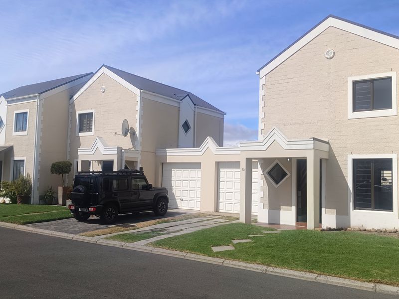 Front elevation of a townhouse complex featuring double garages, paved driveways, and well-maintained lawns under a clear sky.