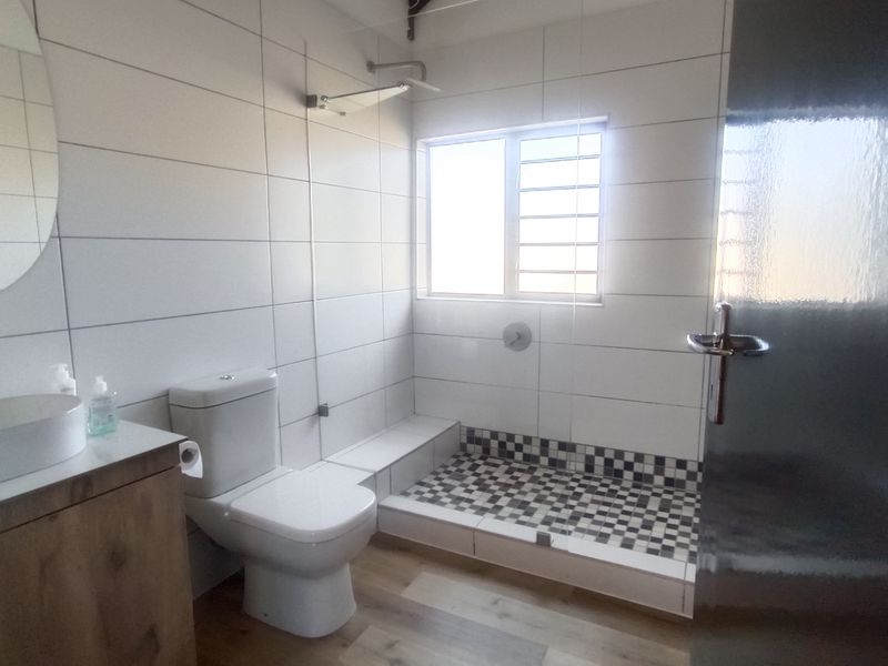 Modern bathroom featuring a walk-in shower with mosaic floor tiles, a vanity with a vessel sink, and clean white wall tiling.