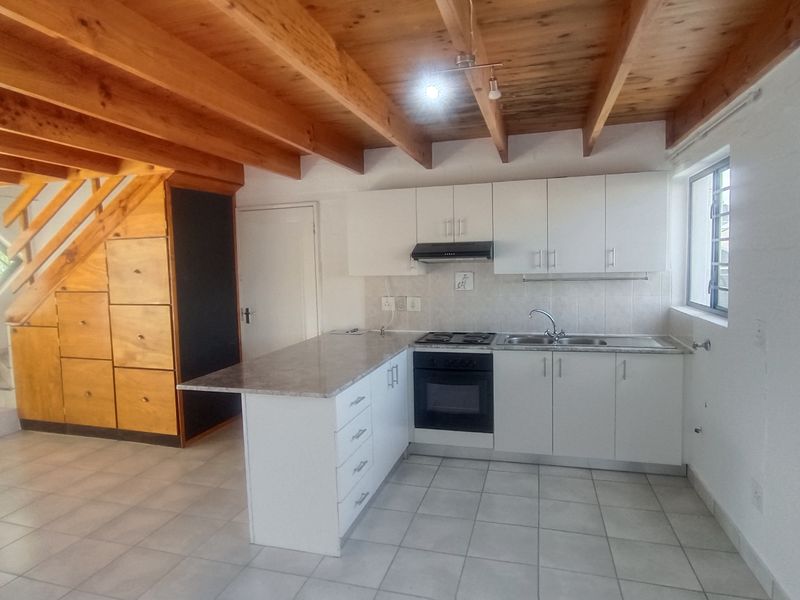 Open-plan kitchen featuring white cabinetry, built-in appliances, and exposed timber ceiling beams, seamlessly integrated with a staircase storage unit and tiled flooring.