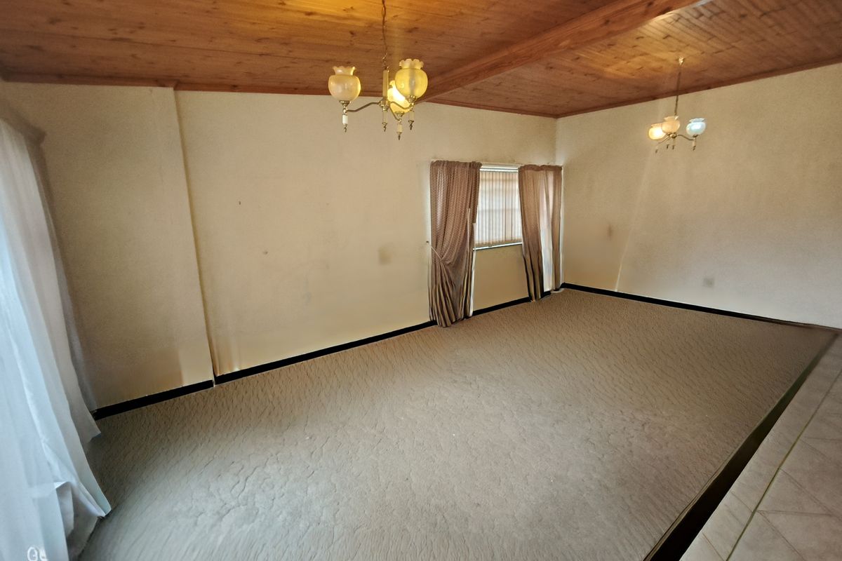 Spacious living area featuring a timber-clad ceiling, fitted chandeliers, and neutral carpeting, offering a blank canvas for interior design updates.