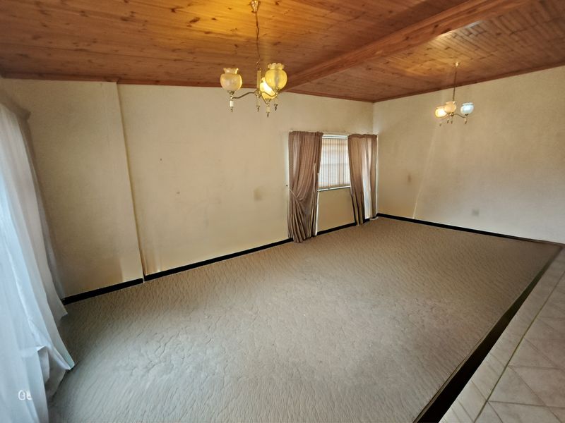 Spacious living area featuring a timber-clad ceiling, fitted chandeliers, and neutral carpeting, offering a blank canvas for interior design updates.