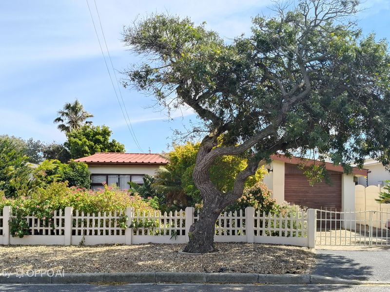 Front view of a residential property featuring a picket fence, mature tree, paved driveway, and a single garage.