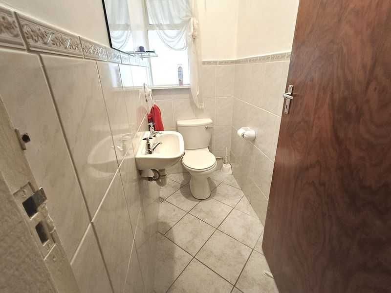 A compact bathroom featuring ceramic wall and floor tiles, a wall-mounted basin, and a standard toilet. The space requires minor maintenance to the door hardware.