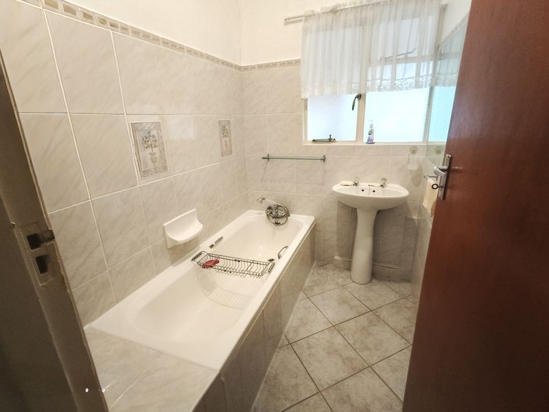 A functional bathroom featuring a built-in bathtub, pedestal basin, and neutral ceramic tiling throughout.