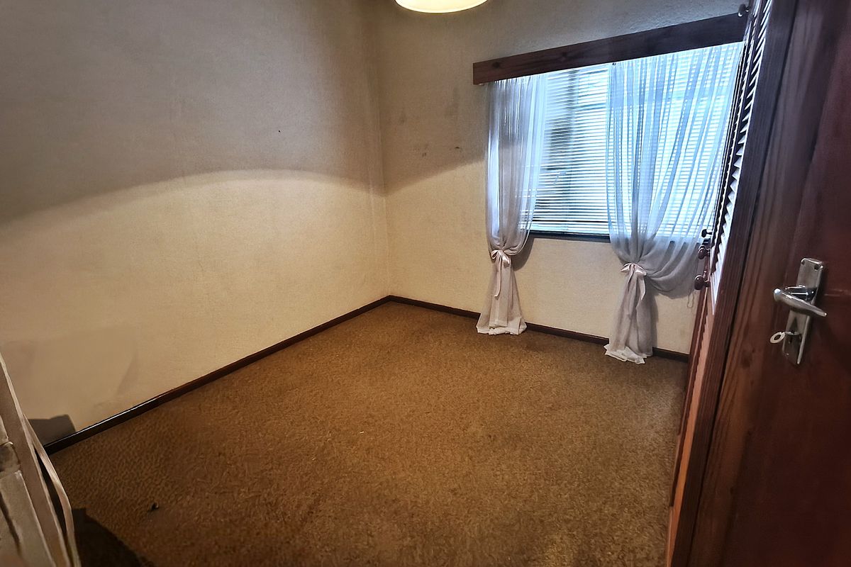 An empty bedroom featuring carpeted flooring, built-in cupboards, and a window with wooden trim, offering a blank canvas for renovation.