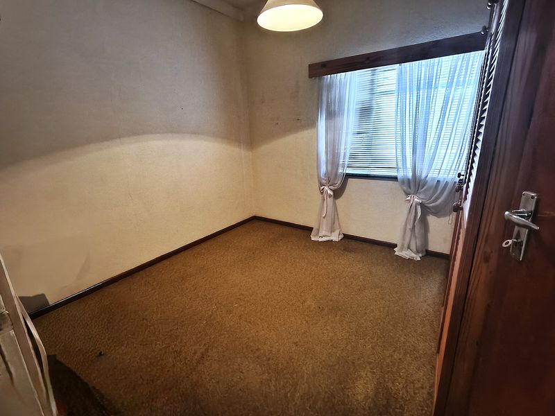 An empty bedroom featuring carpeted flooring, built-in cupboards, and a window with wooden trim, offering a blank canvas for renovation.