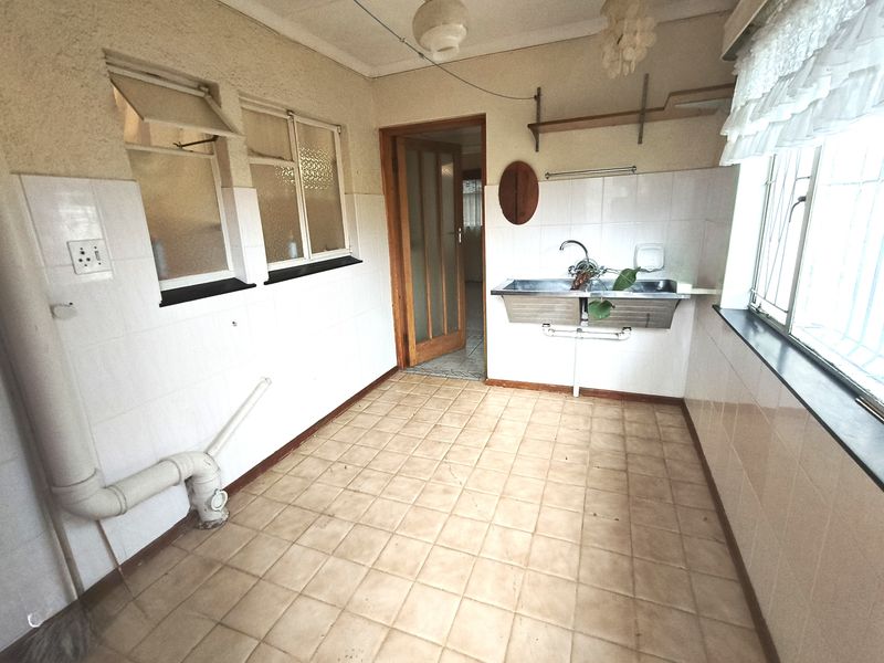 A functional laundry room featuring a double stainless steel sink, tiled walls, and tiled flooring, providing a practical space for utility and washing needs.