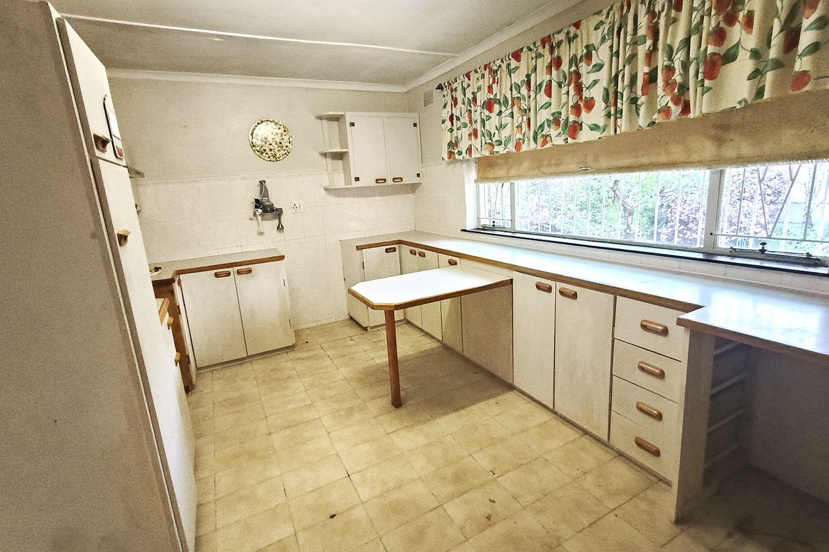 A dated kitchen featuring original laminate cabinetry, tiled flooring, and a built-in breakfast bar, offering significant potential for a modern renovation.