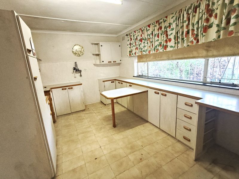 A dated kitchen featuring original laminate cabinetry, tiled flooring, and a built-in breakfast bar, offering significant potential for a modern renovation.