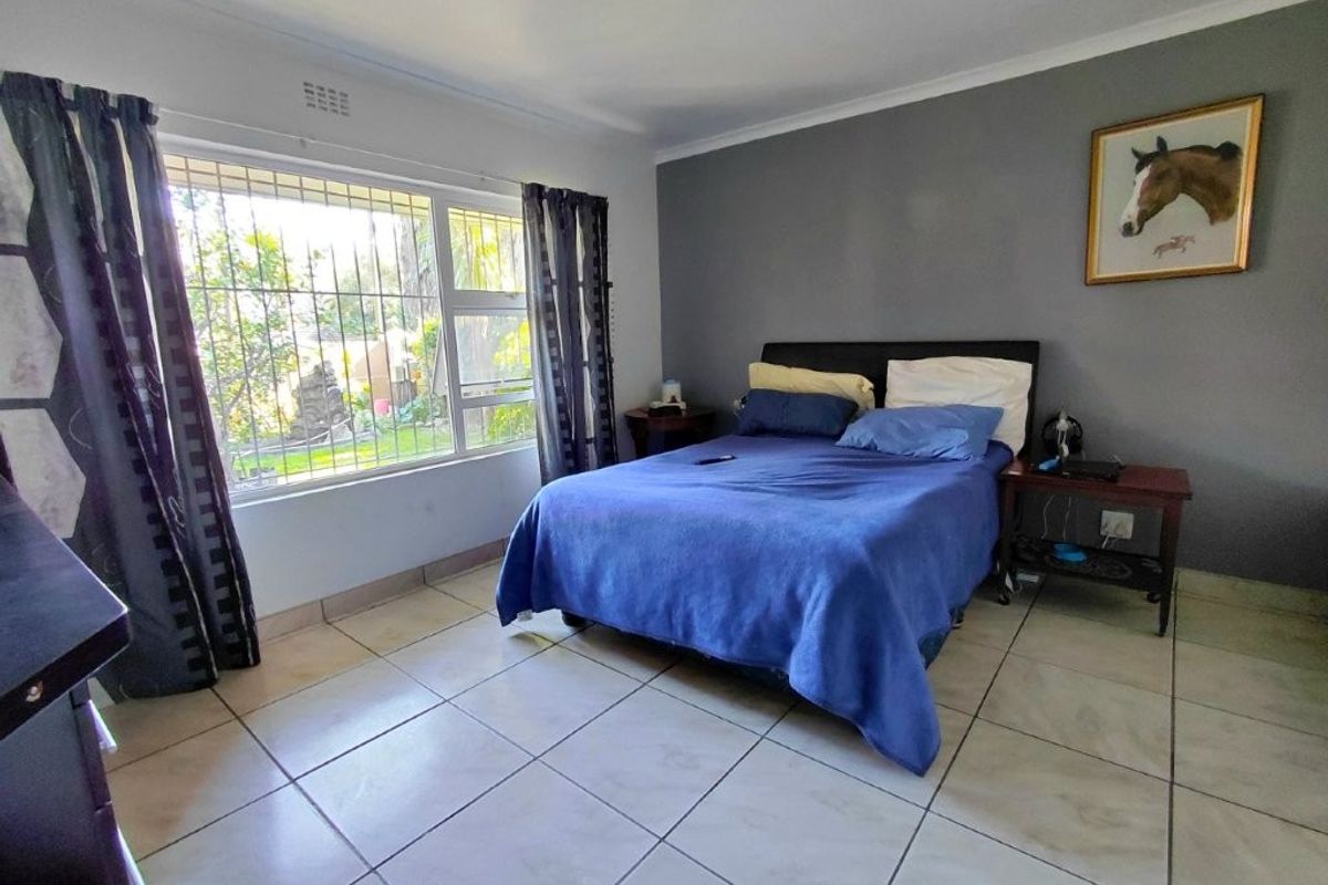 A bedroom featuring tiled flooring, a large window with security bars, and a neutral grey accent wall.