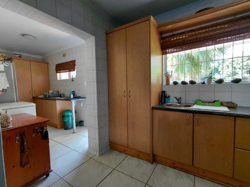 A functional kitchen featuring built-in wooden cabinetry, tiled flooring, and a stainless steel sink, offering a practical layout with potential for modern updates.