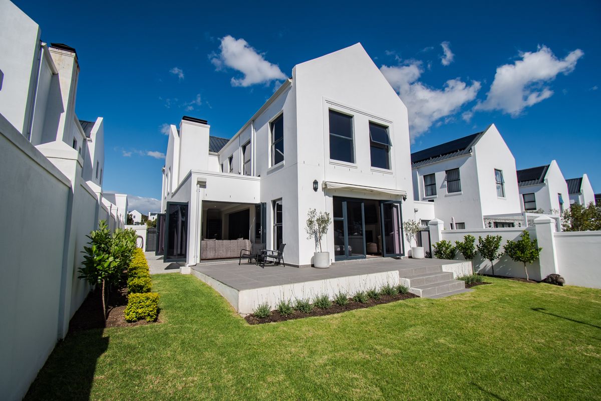 Rear view of a modern home featuring a tiled patio, bi-fold doors, retractable awning, and a well-maintained garden with boundary walls.