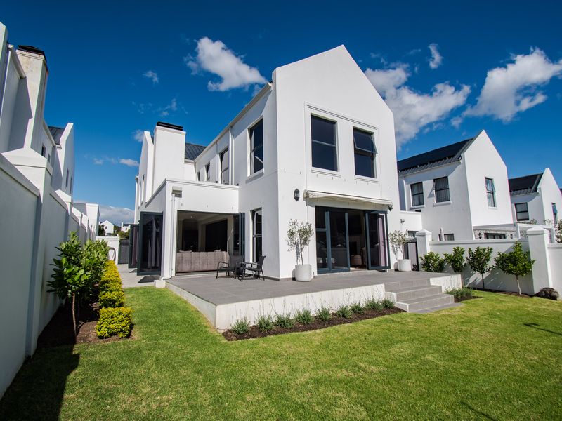 Rear view of a modern home featuring a tiled patio, bi-fold doors, retractable awning, and a well-maintained garden with boundary walls.