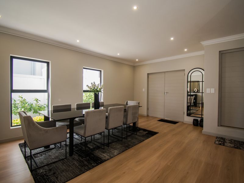 A well-maintained dining room featuring modern laminate flooring, recessed downlighting, and large aluminium-framed windows providing natural light.