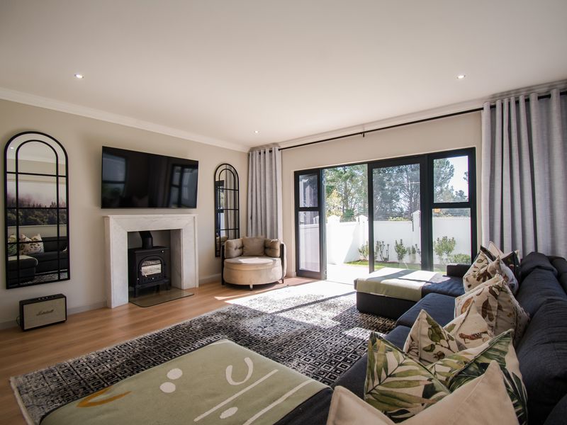 A bright and modern living room featuring a fireplace with a wood-burning stove, laminate flooring, and large sliding doors leading to the garden.