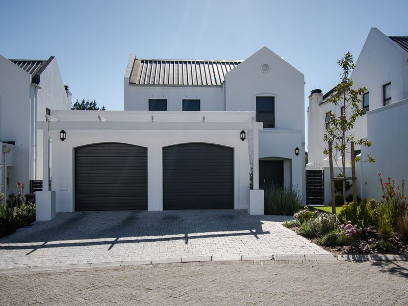 Front elevation of a modern house featuring a double garage with dark roller doors, a pergola structure, and a paved driveway.