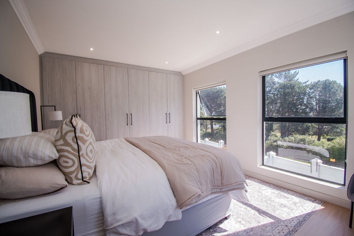 A bright and modern bedroom featuring extensive built-in cupboards, sleek aluminium-framed windows, and high-quality laminate flooring with recessed lighting.