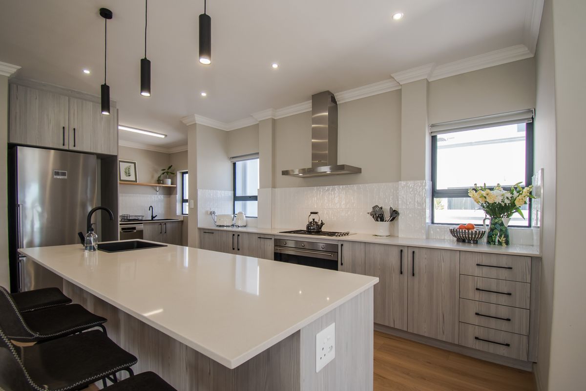 Modern kitchen featuring a large central island with quartz countertops, stainless steel appliances, sleek cabinetry, and stylish pendant lighting.