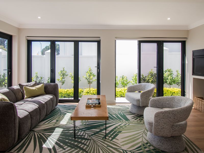 Modern living room featuring timber flooring, recessed downlights, and black aluminium bifold doors providing seamless access to the garden area.